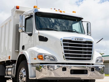 Close-up of the front grille of a heavy-duty, branded roll-off truck, clean and powerful, under crisp Miami sunlight, low-angle heroic shot.