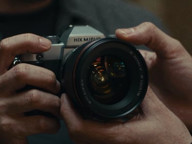 Cinematic film still, extreme close-up of hands adjusting a high-end camera lens, dramatic chiaroscuro lighting, rich graded shadows, 35mm grain