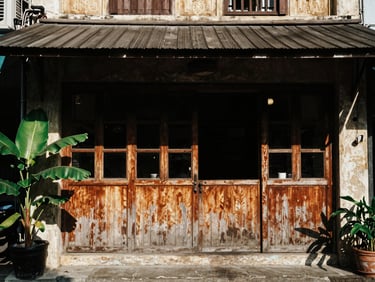 An environmental documentary shot of a rustic cafe storefront in Saigon, weathered wood, heavy shadows, tropical foliage.