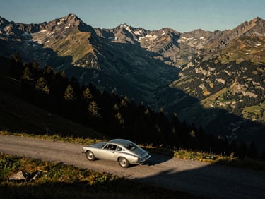 A classic car or motorcycle on the Furka Pass, viewed from above, with dramatic mountain peaks and deep valleys in the background, moody lighting.