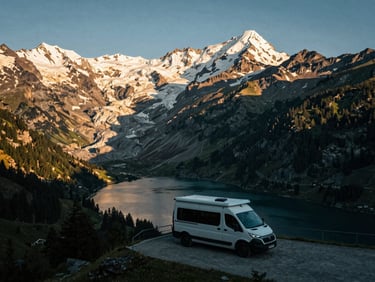 A campervan (Spartacus) parked at a viewpoint on Susten Pass, overlooking a glacial lake and snow-capped peaks, early morning light.