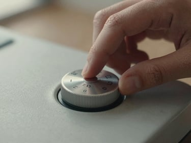 Close-up of hands interacting with a physical, weighted metal dial on a matte ceramic surface, soft natural afternoon light.