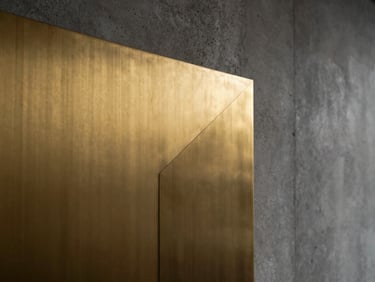 A close-up of a brushed brass wall panel with a razor-thin, warm light projection glowing along its geometric seam, low-key dramatic architectural lighting, raw concrete texture behind.