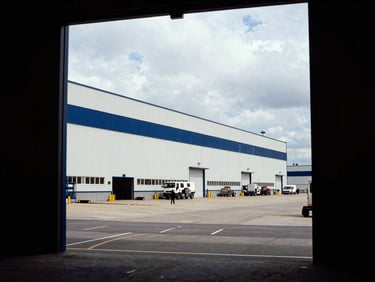 Wide environmental shot of a massive logistics hub with integrated energy assets, clean architectural lines, overcast daylight, human figure at a distance for scale.