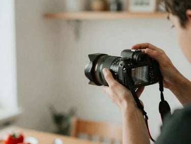 Candid environmental shot of a person shooting food photography with a professional camera, soft diffused side-light, shallow depth of field.