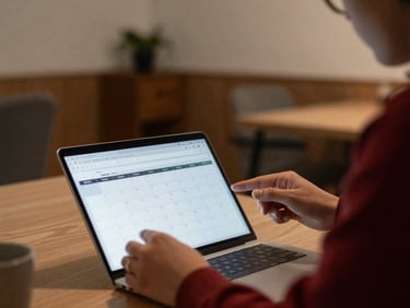 Candid environmental shot of a person reviewing content calendar on a laptop, soft warm indoor ambient light, cozy office setting.
