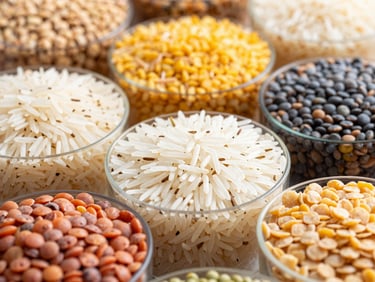 Close-up of various grains and pulses in clear containers, including basmati rice and lentils, natural daylight, crisp focus.