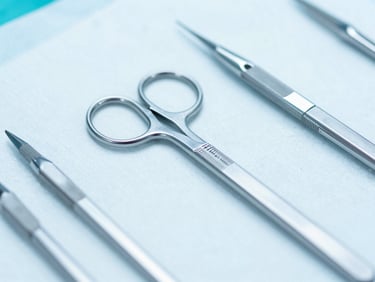Close-up macro shot of sterile surgical blades and needles on a clean clinical surface, bright high-key lighting, cool blue tones