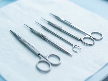 Sharp macro shot of sterile surgical blades and steel needles arranged neatly under high-key clinical lighting.