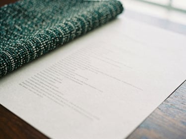 Close-up of tactile woven tweed fabric and heavy textured paper brand guidelines on a dark oak table, soft window light, shallow depth of field