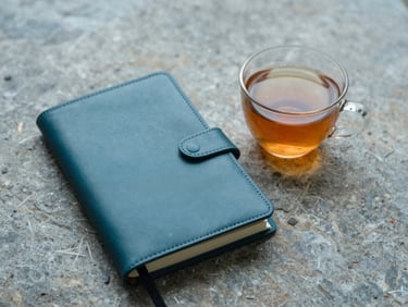 A clean leather journal open next to a warm cup of tea on a rustic stone surface, soft overcast lighting.