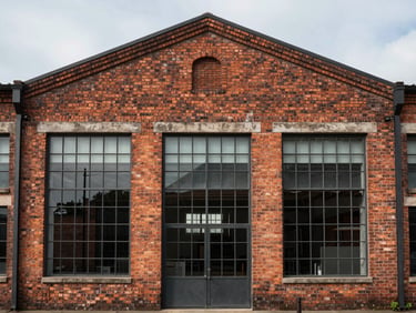 Straight-on architectural elevation of a restored brick warehouse with large steel-framed windows under soft overcast daylight