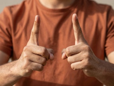 Close-up of a person's hands forming a clear sign, warm dramatic side lighting, shallow depth of field, terracotta color accents.