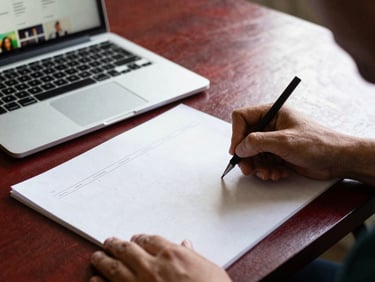 Hands sketching content calendars on a table with a laptop displaying social media feeds, soft natural side-light, deep red and forest green tones, shallow depth of field, 35mm, authentic agency moment
