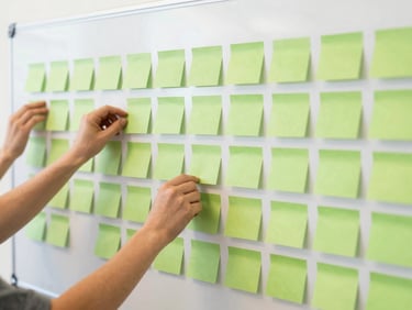 Close-up of hands placing colorful sticky notes on a large planning board during a community workshop, bright lighting.
