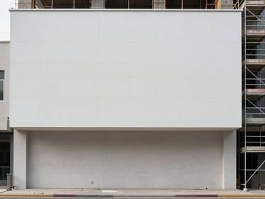 Wide shot of a commercial building facade mid-execution, scaffolding visible to the right third, fresh render on the upper half contrasting with bare substrate below, diffused daylight, no people in frame