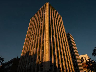 Fachada imponente de edificio corporativo moderno en Paseo de la Reforma, Ciudad de México, con reflejos dorados del atardecer, ángulo bajo, dramático, 35mm.
