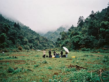 moody cinematic film photography, wide panoramic shot of an outdoor film set in a misty green valley, small crew working under an overcast sky