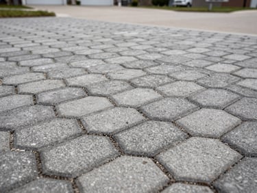 Close-up overhead shot of freshly installed interlocking permeable pavers with tight seams, dark sand infill visible, natural overcast daylight, suburban driveway edge in background