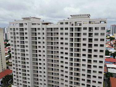 Wide shot of a completed mid-rise residential building exterior under overcast São Paulo sky, aerial perspective showing full structural volume and façade geometry, surrounding urban context visible, no people, documentary framing