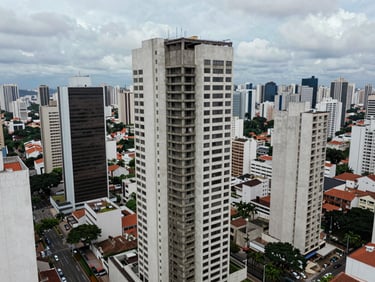 Wide aerial view of a completed commercial high-rise in the São Paulo metropolitan area, structural concrete core visible at rooftop, overcast diffuse light, surrounding urban context in frame, no people