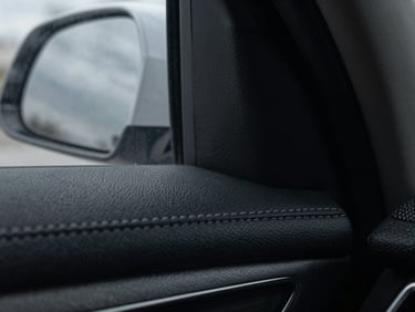 Macro detail of leather stitching on a pristine executive sedan interior, cool overcast daylight reflecting off the window, desaturated dark tones