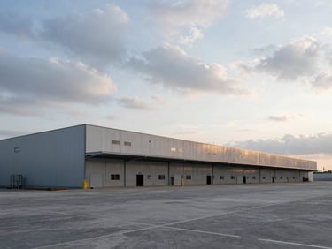 Wide-angle perspective of a massive logistics warehouse under construction, dramatic overcast sky, cool morning light