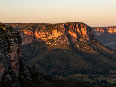 Wide panoramic view of the red cliffs of Chapada dos Guimarães during golden hour, deep green valleys below, warm editorial light.
