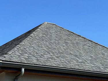 Low angle shot of a clean, newly shingled roof peaking against a bright blue sky with modern gutters.