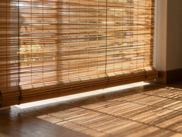 Close-up of hand-woven bamboo blinds filtering warm afternoon sunlight onto a polished drawing room floor, creating soft shadows.