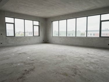 Wide environmental shot of a freshly cleaned empty room after construction — bare concrete floor swept clean, large windows letting in overcast daylight, no dust, no debris