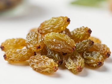 Macro shot of premium sun-dried golden raisins piled on a clean white surface, soft natural light.