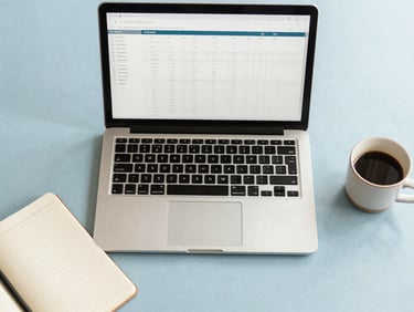 Overhead flat-lay of an organized modern desk with a sleek laptop showing clean spreadsheets, a neat notebook, and a ceramic coffee cup in soft morning light.