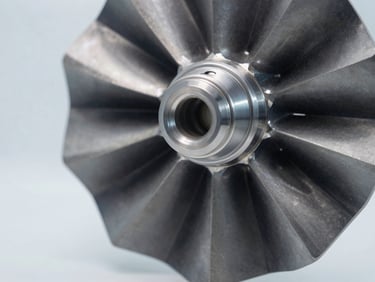 Macro detail shot of a machined aluminum turbine blade, cool laboratory lighting, deep gray and metallic silver tones.