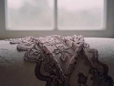 Close-up of intricate, dark lace draped over a smooth, pale stone, gentle shadows, overcast window light, muted rose and charcoal tones, shallow depth of field, 35mm