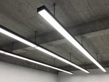 Straight-on structured shot of modern architectural linear LED lighting fixtures mounted on a concrete ceiling, crisp high-contrast light