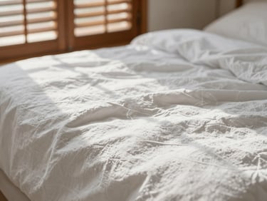 Close-up of crisp white linen sheets with natural creases, soft morning light filtering through wooden shutters, warm and serene.