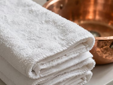 Tactile close-up of heavy, unbleached cotton towels resting beside a copper water basin, soft shadows.