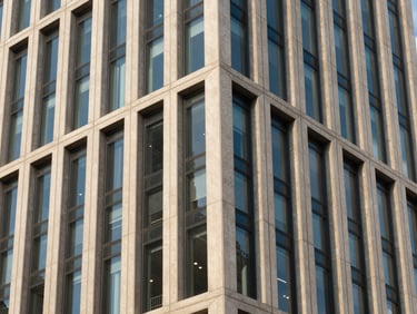 Crisp architectural photography of a modern financial center facade, sharp geometric patterns in building concrete and glass, bright daylight with cool blue and warm golden-hour highlights, 35mm lens.