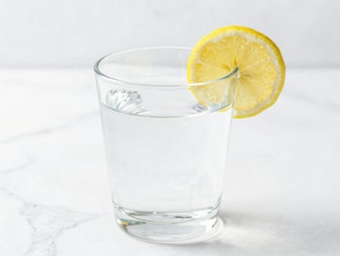 Bright high-key photography, soft natural daylight, a clear glass of pure water with a lemon slice on a white marble background, crisp details.