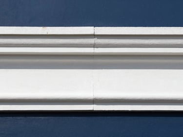 Crisp architectural photography of a perfectly mitered white crown molding joint against a deep navy wall, bright natural daylight, 35mm