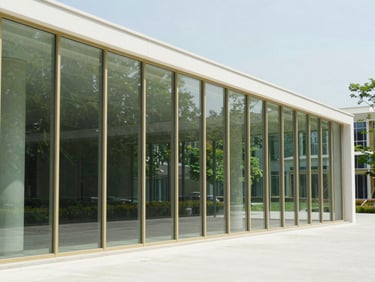 Clean architectural detail of a modern tech campus glass pavilion reflecting bright daylight and green foliage.