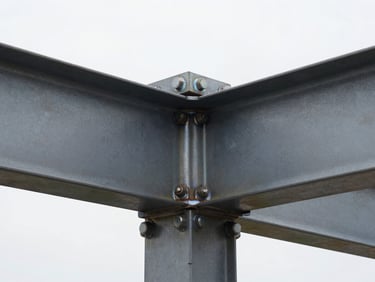 High-contrast close-up of a structural steel connection with heavy bolts and clean welds, industrial daylight highlighting the raw steel texture.