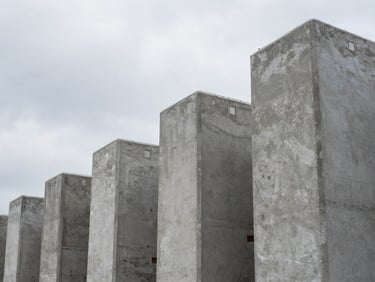 Close-up overhead shot of stacked precast concrete columns on a construction yard, grade markings visible on the faces, overcast natural daylight, no people