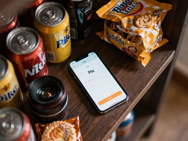 Close-up overhead flat-lay of a compact office microstore shelf: canned drinks, snacks, and a smartphone showing a Pix payment confirmation screen, natural indoor light, dark wooden surface