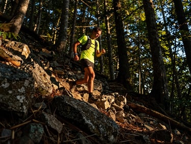 Trail runner navigating a steep, rocky forest path at golden hour, dynamic low-angle, high-contrast, sweat visible.