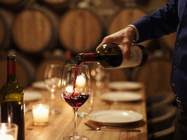 Close-up of a sommelier pouring red wine into a glass, dimly lit cellar with warm golden lighting, elegant atmosphere