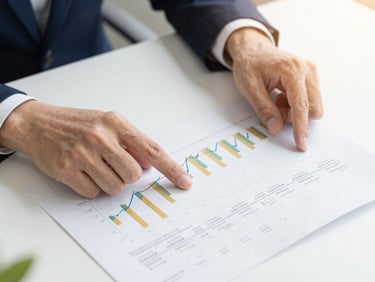 Close-up of professional hands pointing to financial growth charts and tax documents on a clean, modern office desk, warm daylight