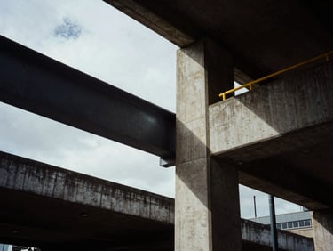 Low-angle architectural shot of concrete and steel structures in East London, high-contrast shadows, overcast daylight.