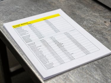 Tight macro detail of a heavy-stock printed brand manual on an industrial steel table, sharp yellow accent ink visible.